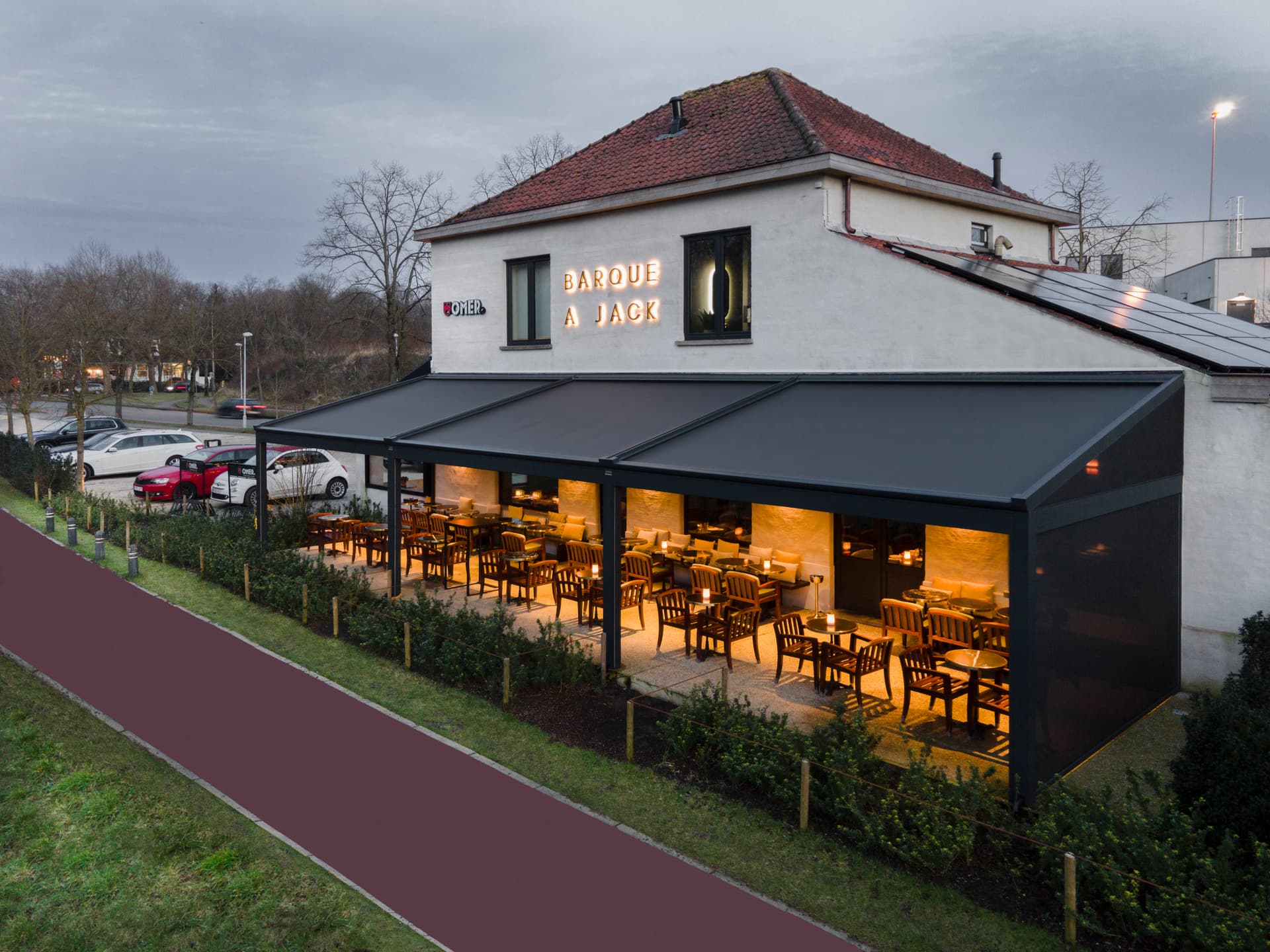 Aluminium B128 XL‑pergola met volledig uitgerold doekdak boven een warm verlicht restaurantterras met houten buitenmeubilair
