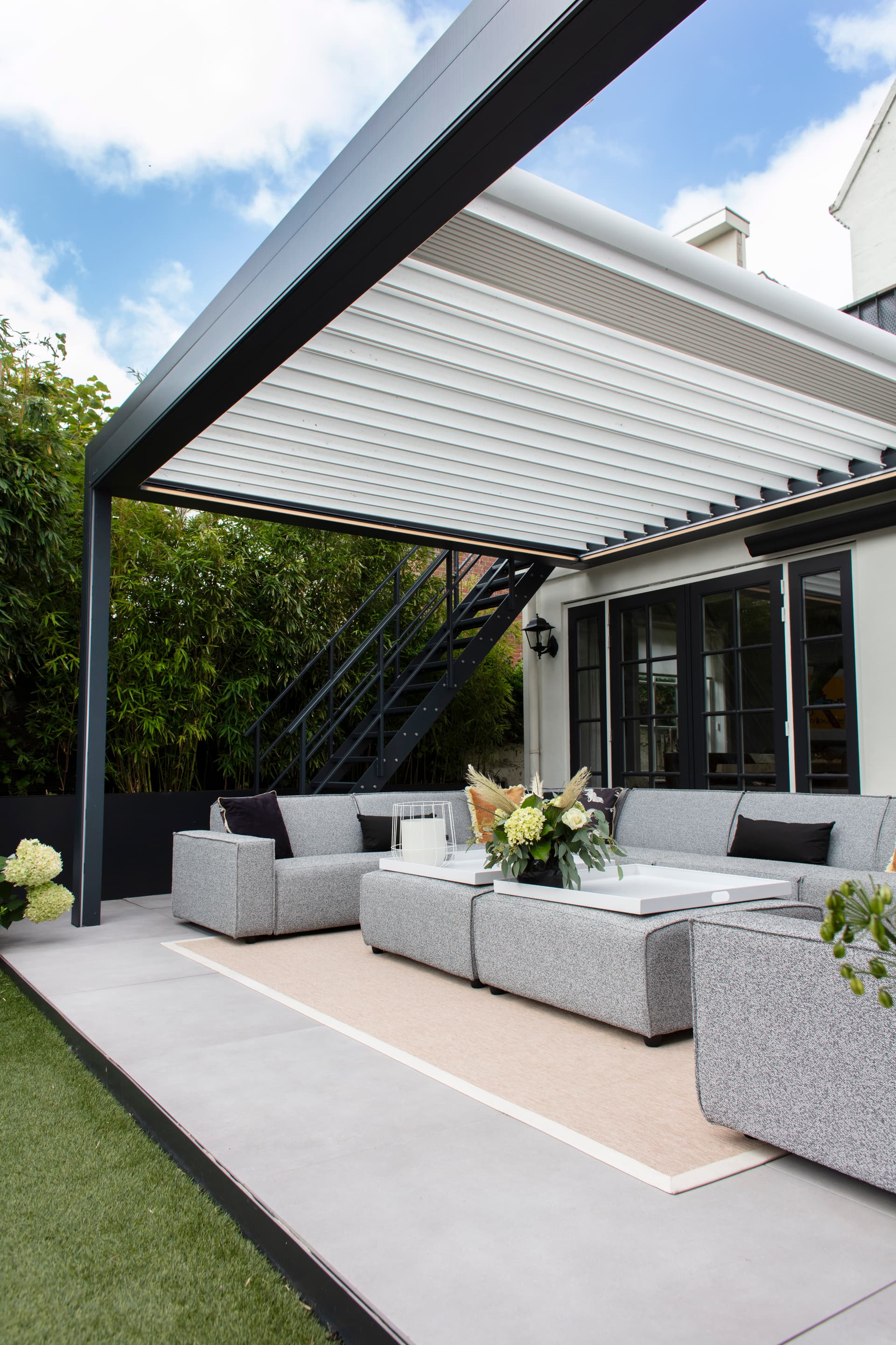 Aluminium terrasoverkapping met openschuifbaar lamellendak boven een moderne loungeset naast de woning