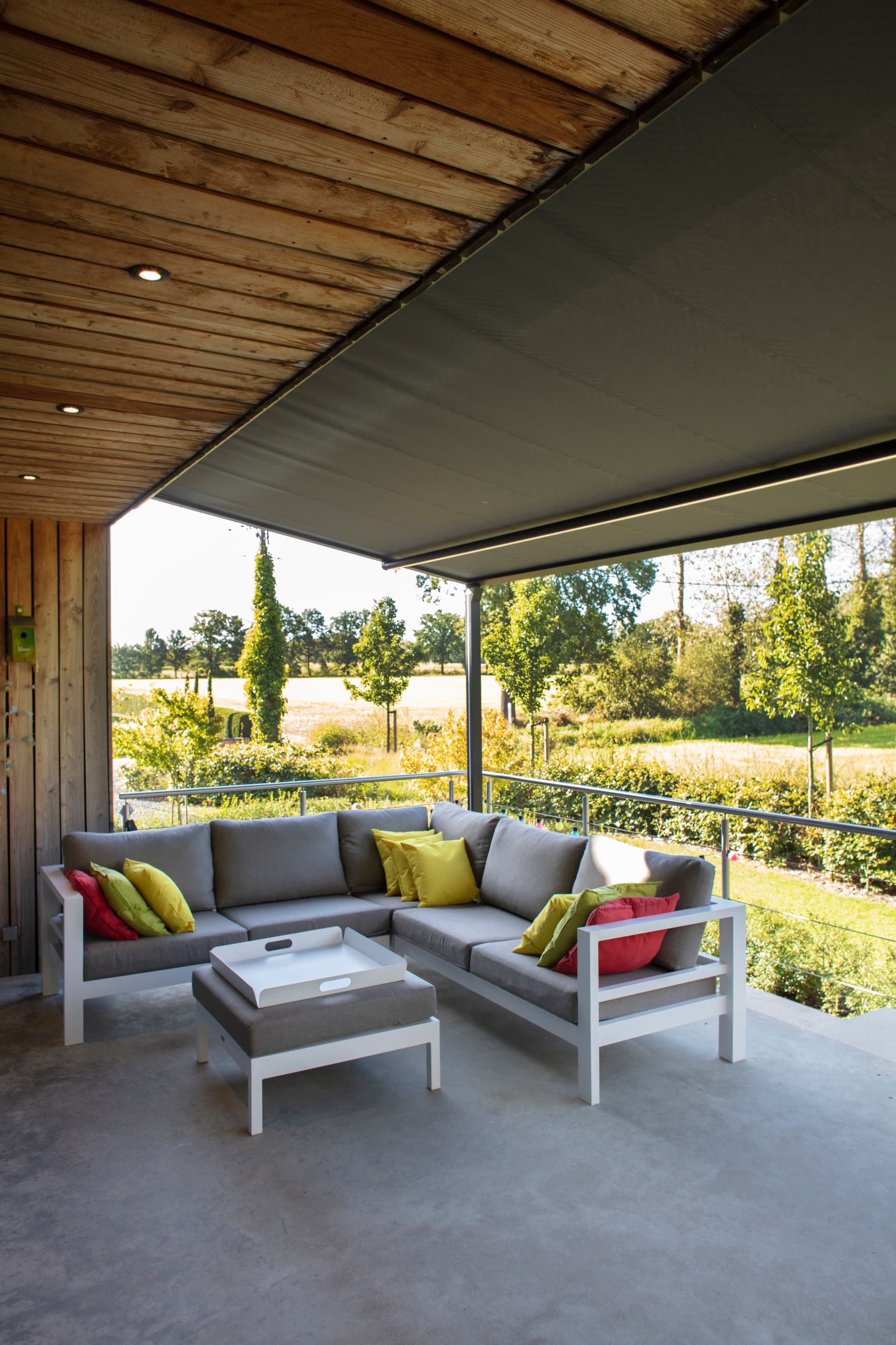 Aluminium pergola met oprolbaar doekdak boven een moderne loungehoek met uitzicht op een zonnige tuin en open landschap