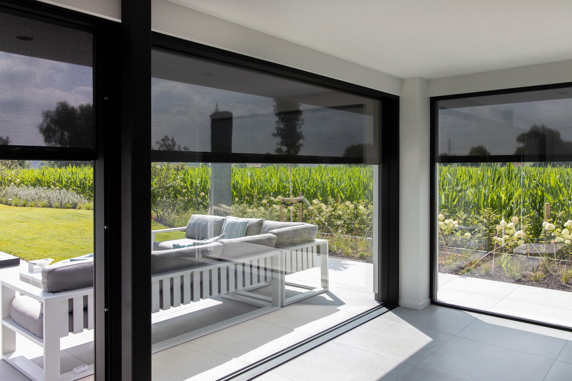 ZIP‑screens in donkere uitvoering aan grote schuiframen van een moderne woning met zicht op de tuin