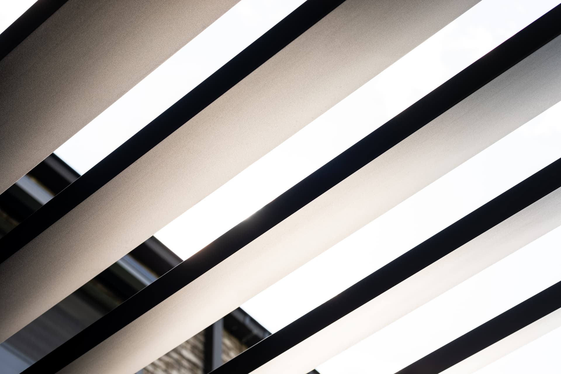 Close‑up van aluminium lamellen van een pergola, van onderaf gezien, met licht dat tussen de open lamellen valt.