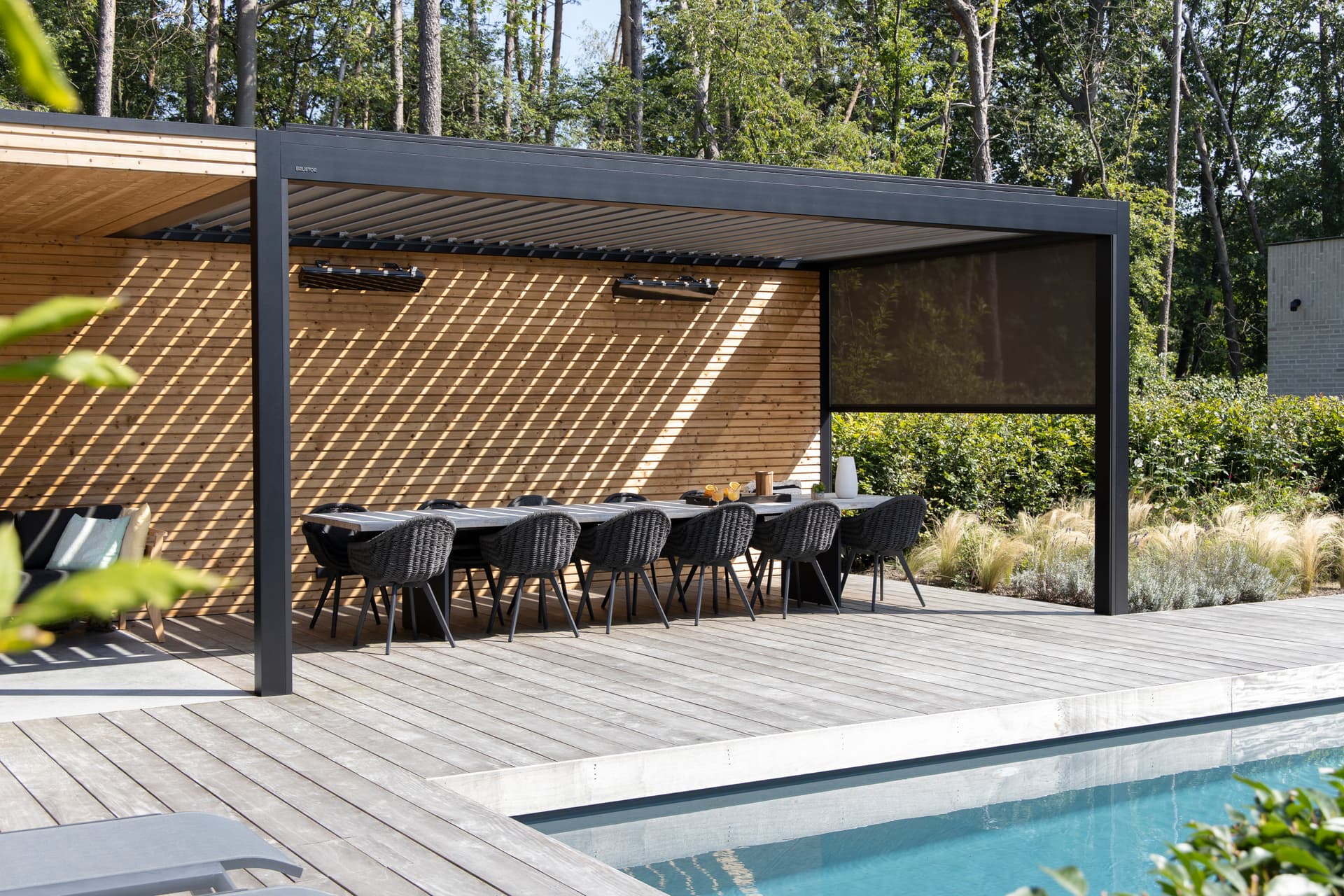 Aluminium pergola met lamellendak en ZIP‑screen die een buiteneethoek overschaduwt naast een houten terras en zwembad.