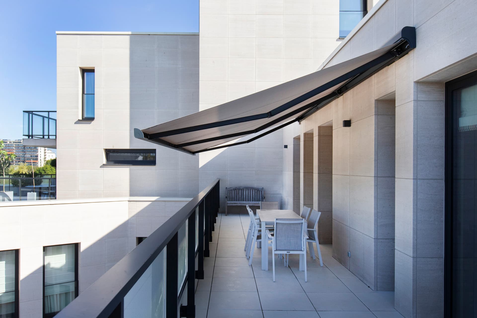 Brustor B25 knikarmscherm dat schaduw creëert boven een modern balkon met buiteneettafel aan een strakke gevel