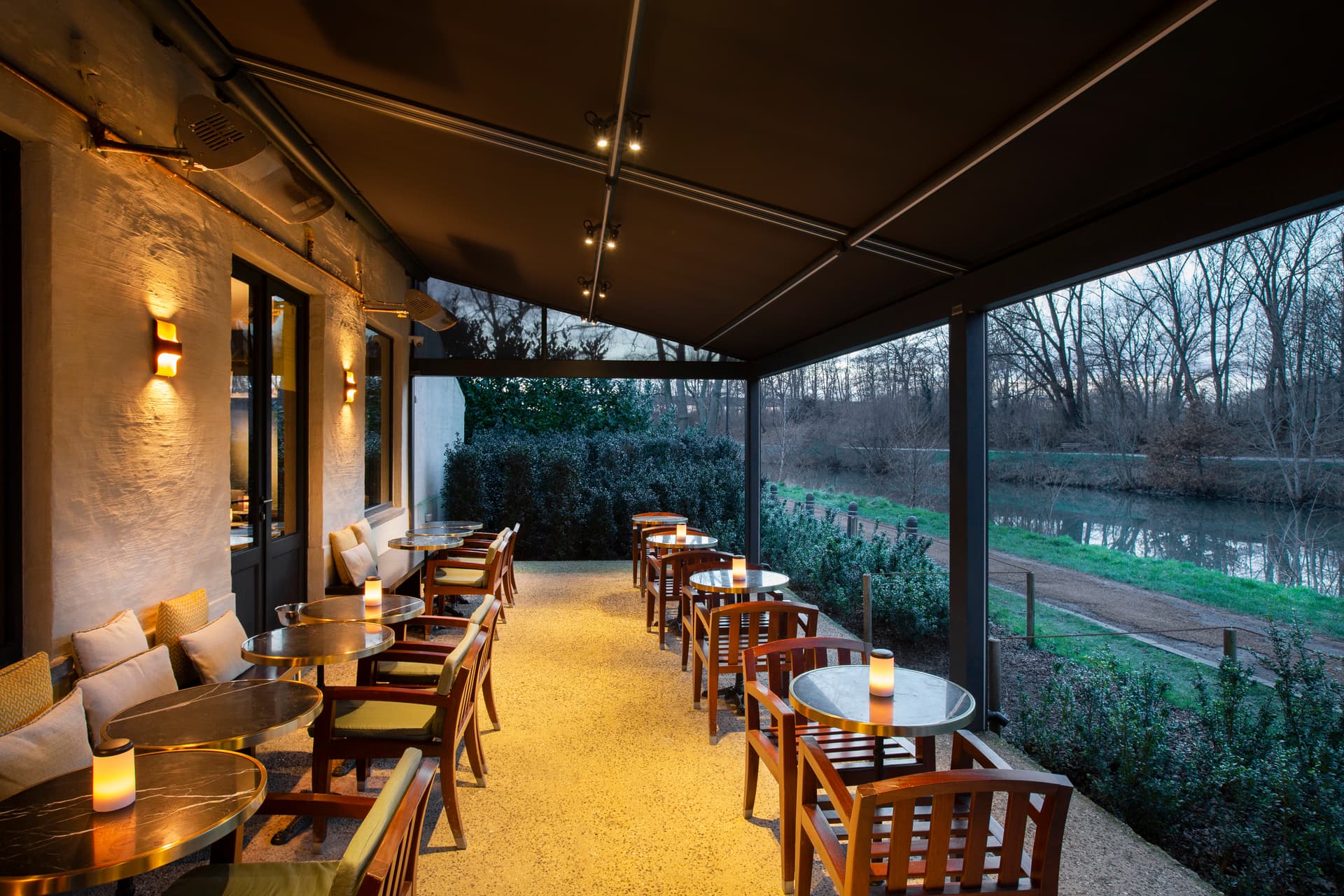 Aluminium B128 XL‑pergola met oprolbaar doekdak en geïntegreerde spots boven een sfeervol restaurantterras met houten zitmeubilair