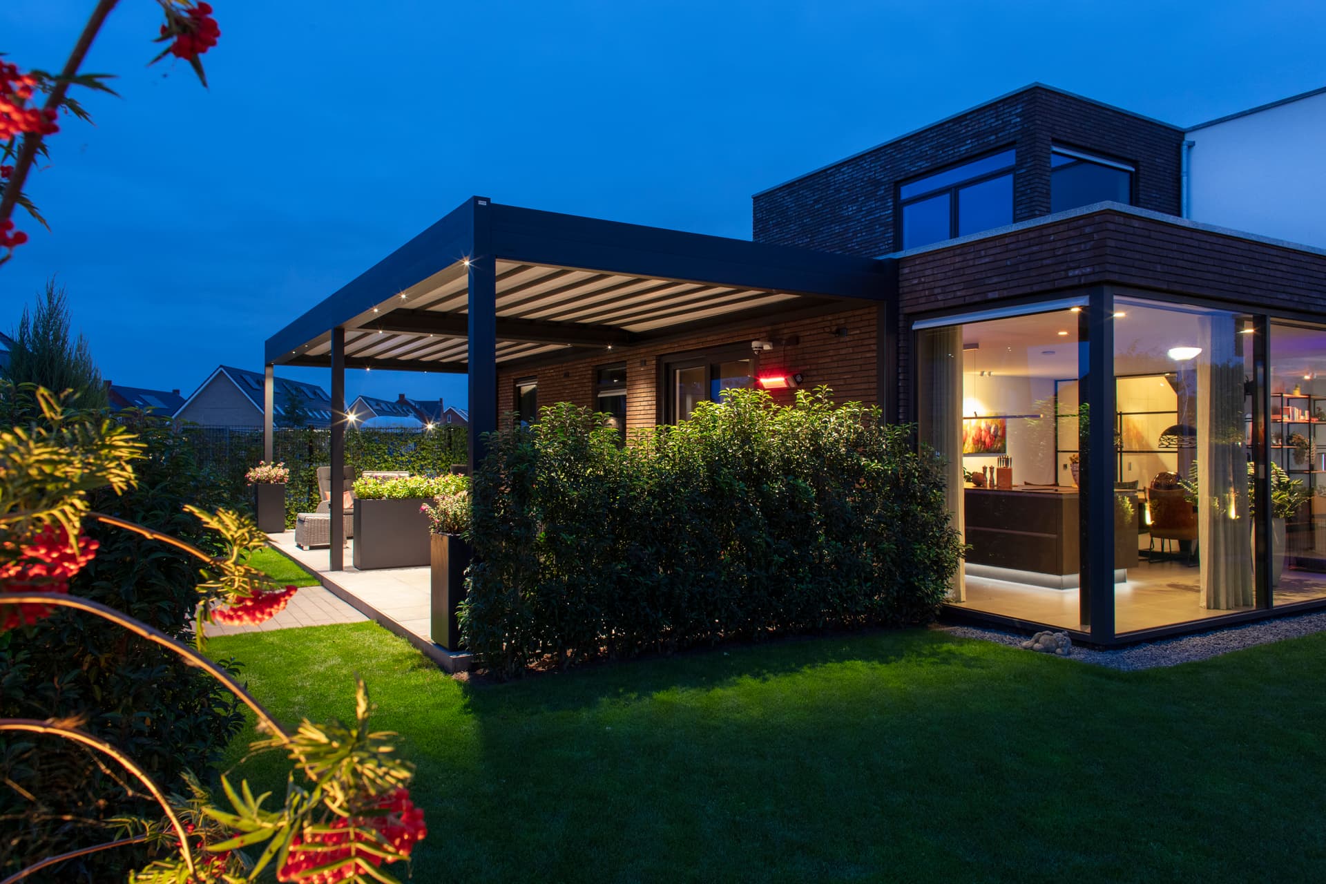 Aluminium B300‑pergola met deels geopend harmonicadoek en warme avondverlichting boven een moderne lounge‑ en eethoek in de tuin