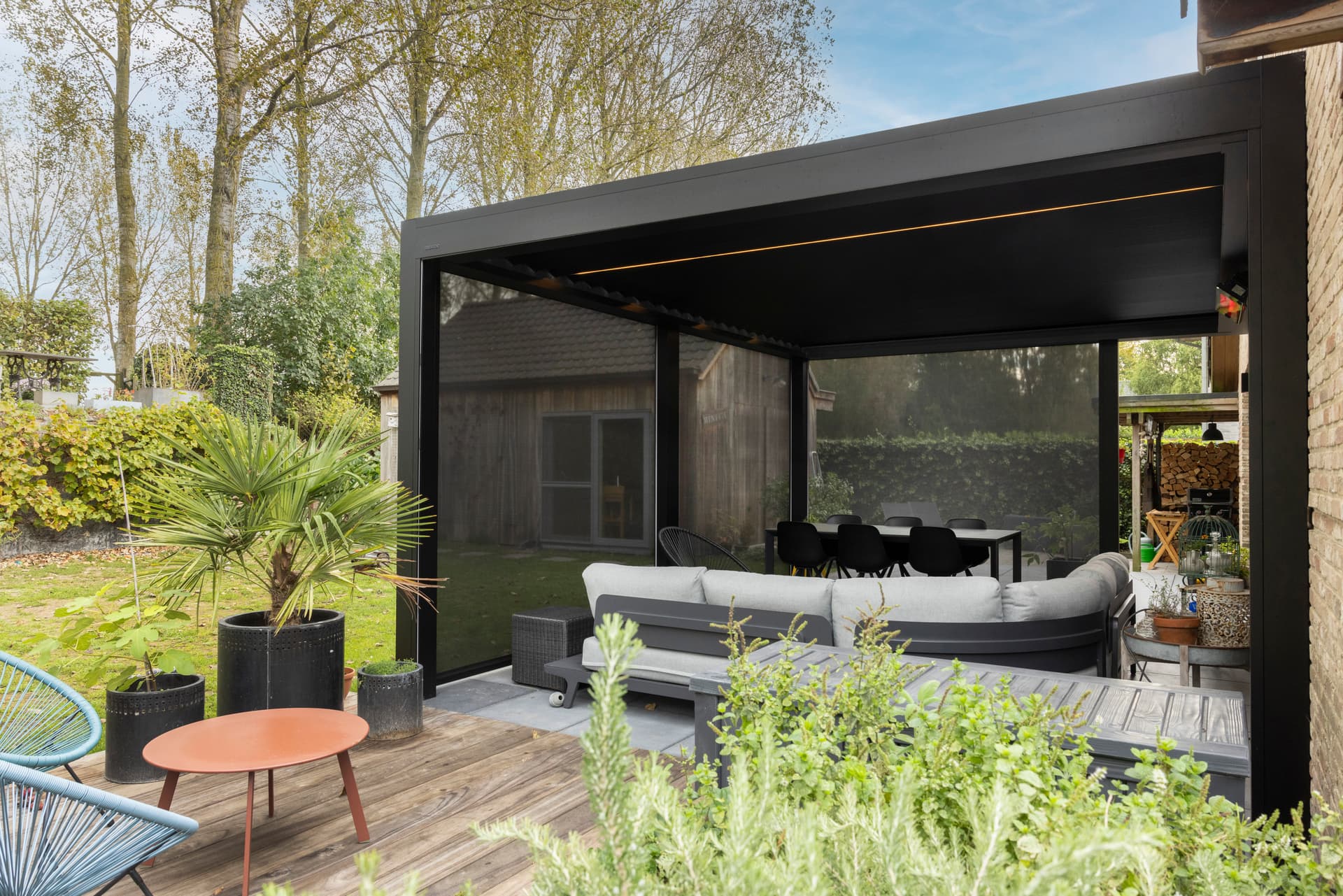 Aluminium louvred roof pergola with ZIP screens in dark finish installed in contemporary garden with lounge and dining area