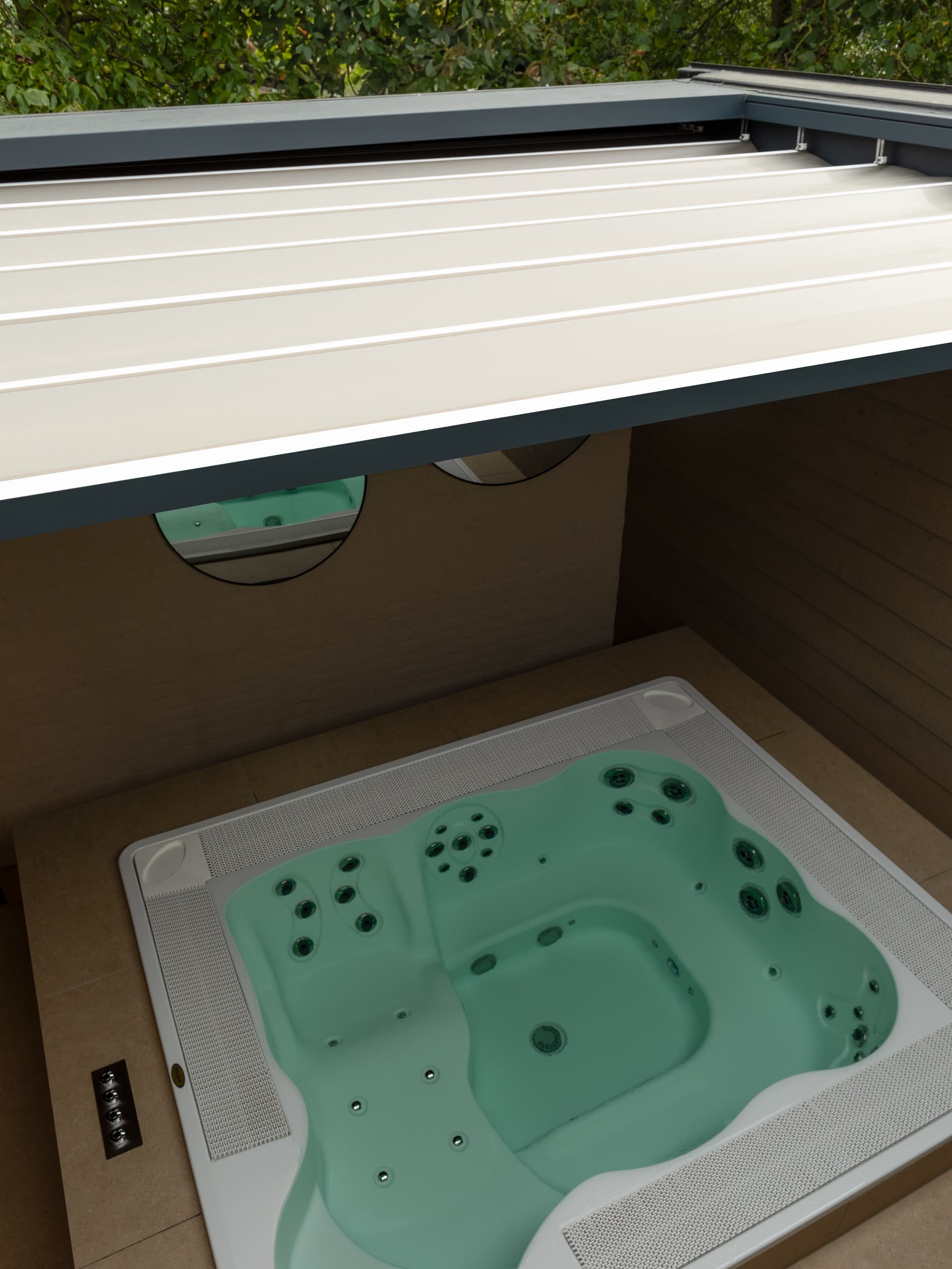 Aluminium B300‑pergola met harmonicadoek boven een moderne jacuzzi in een serene wellnessruimte met houten afwerking