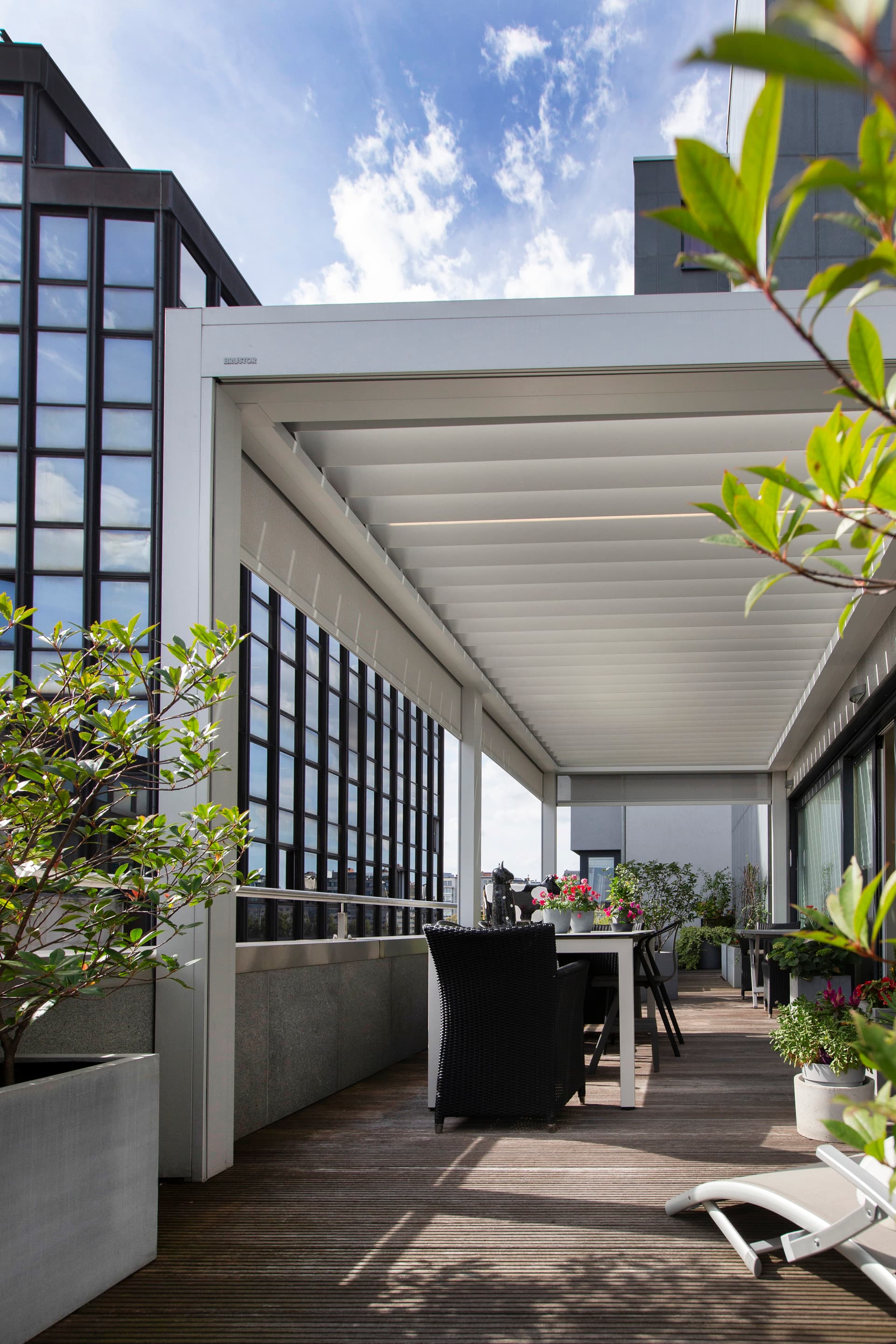 Brustor‑Pergola mit Lamellendach, die einen schattigen Essbereich im Freien auf einer großzügigen Apartmentterrasse mit Stadtblick schafft