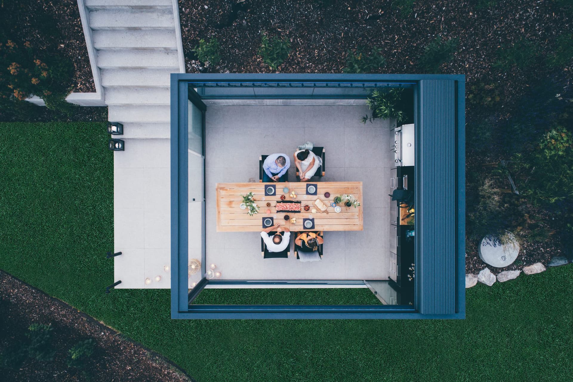Bovenaanzicht van aluminium terrasoverkapping met openschuifbaar lamellendak boven een moderne buiteneettafel in groene tuin