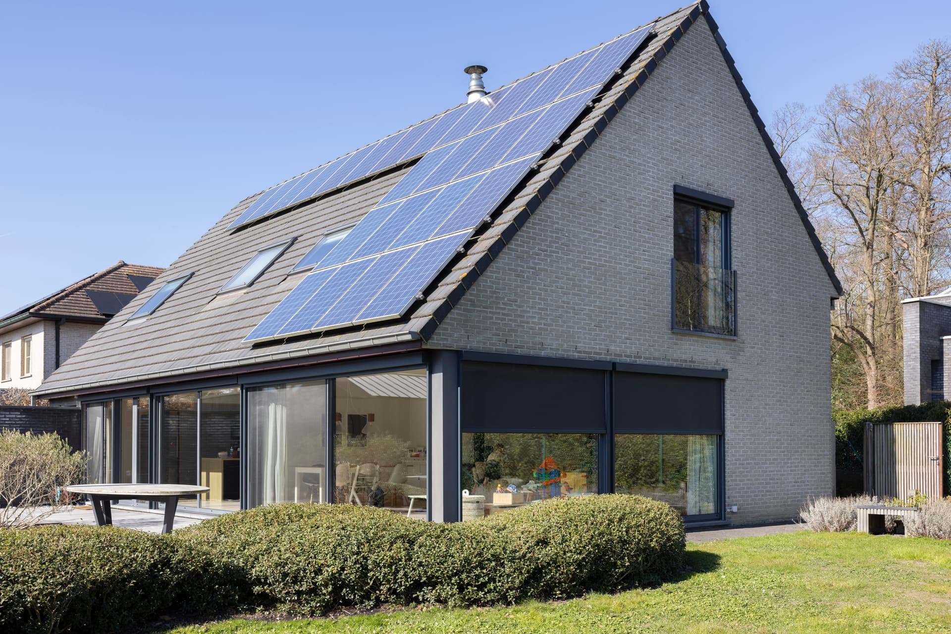 Moderne gelijkvloerse woning met grote schuiframen en buitenzonwering met uitzicht op een groene tuin.
