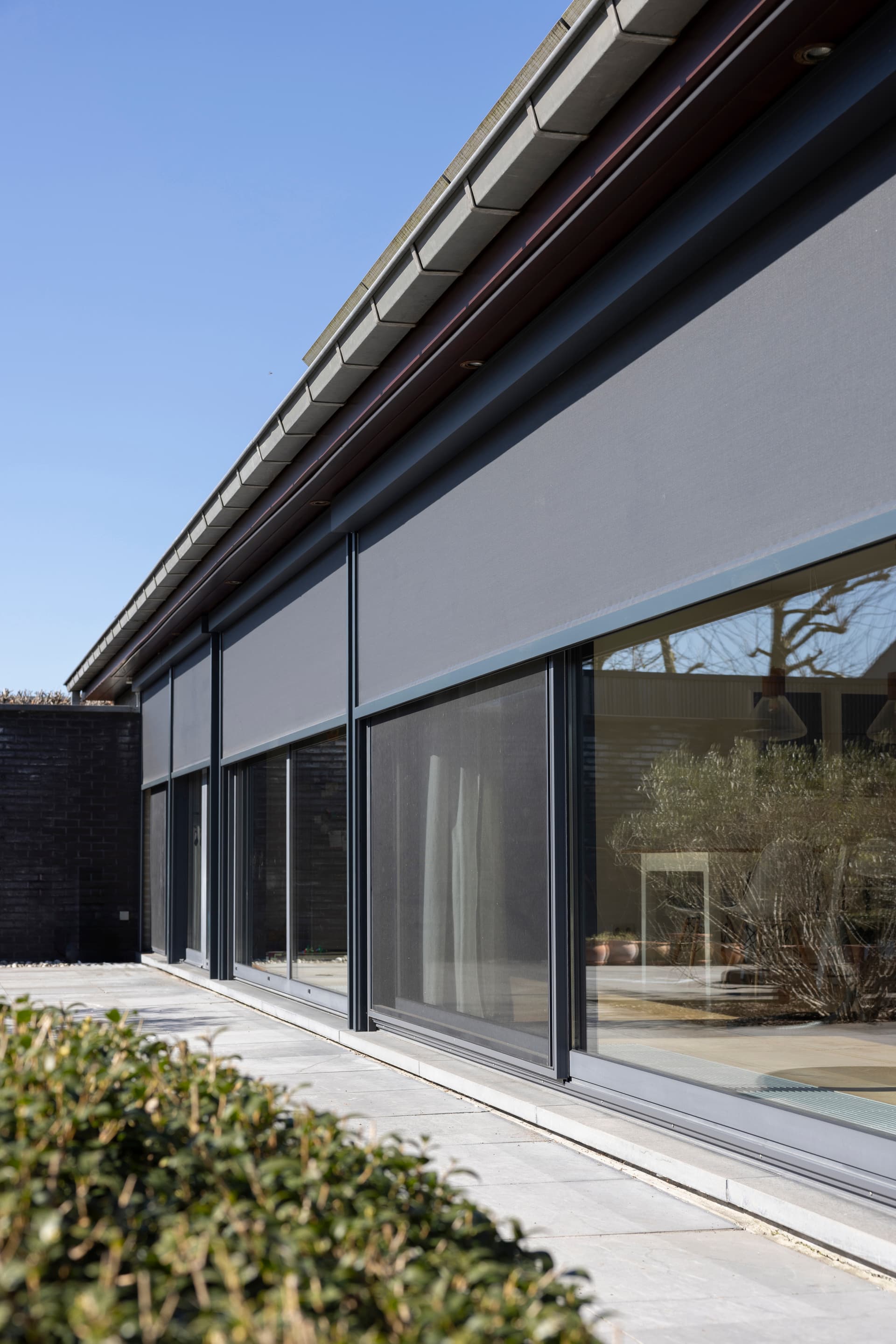 Moderne gelijkvloerse woning met grote schuiframen en buitenzonwering met uitzicht op een groene tuin.