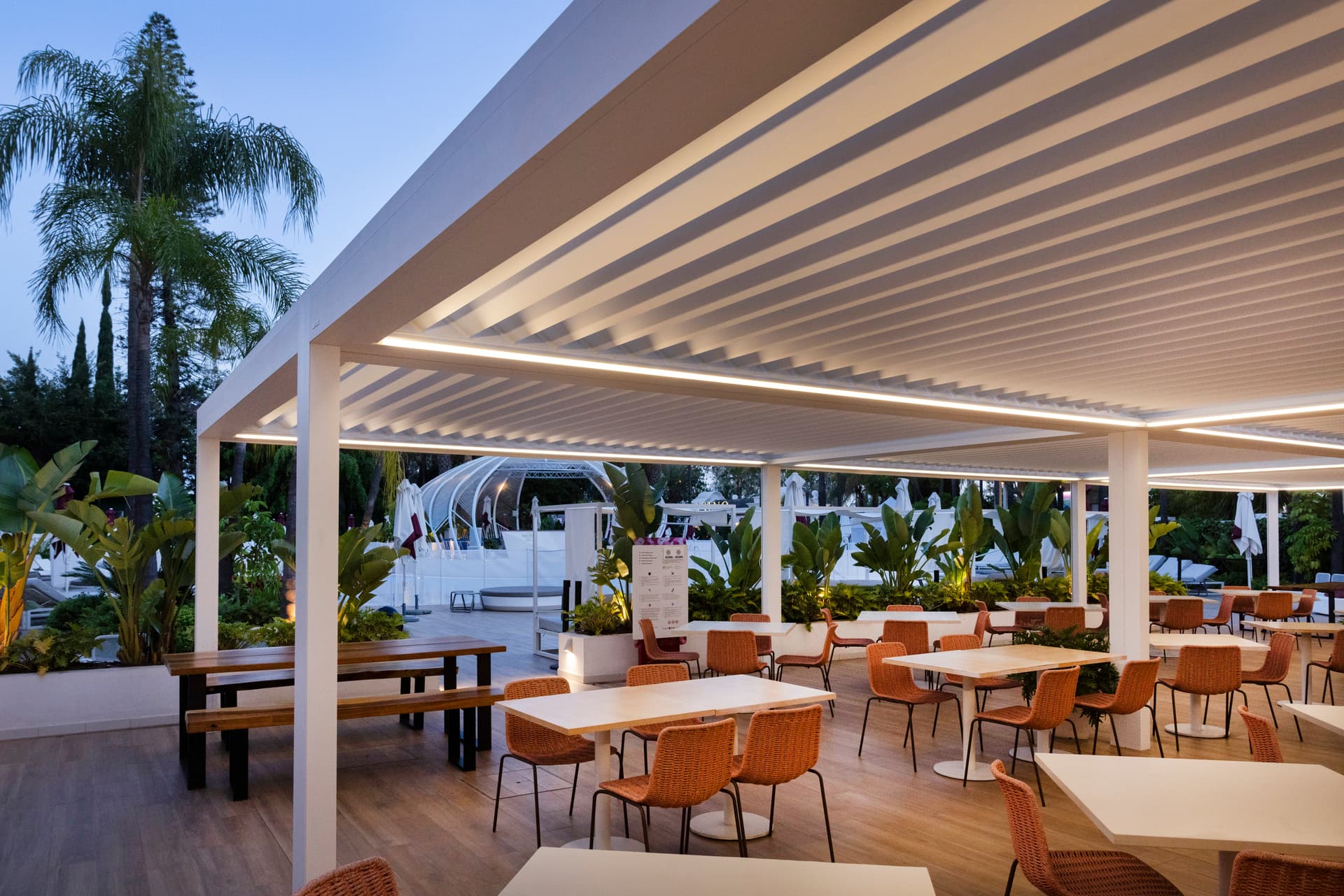 Aluminium pergola met lamellendak en geïntegreerde ledverlichting boven een buitenterras met horecazitplaatsen.