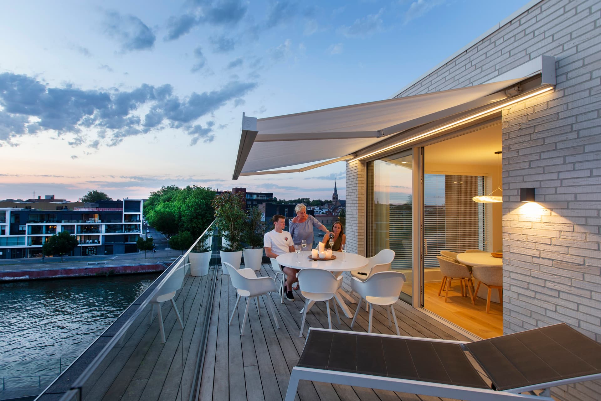 Aluminium retractable awning creating shade over a modern rooftop dining terrace with evening ambiance and waterfront view