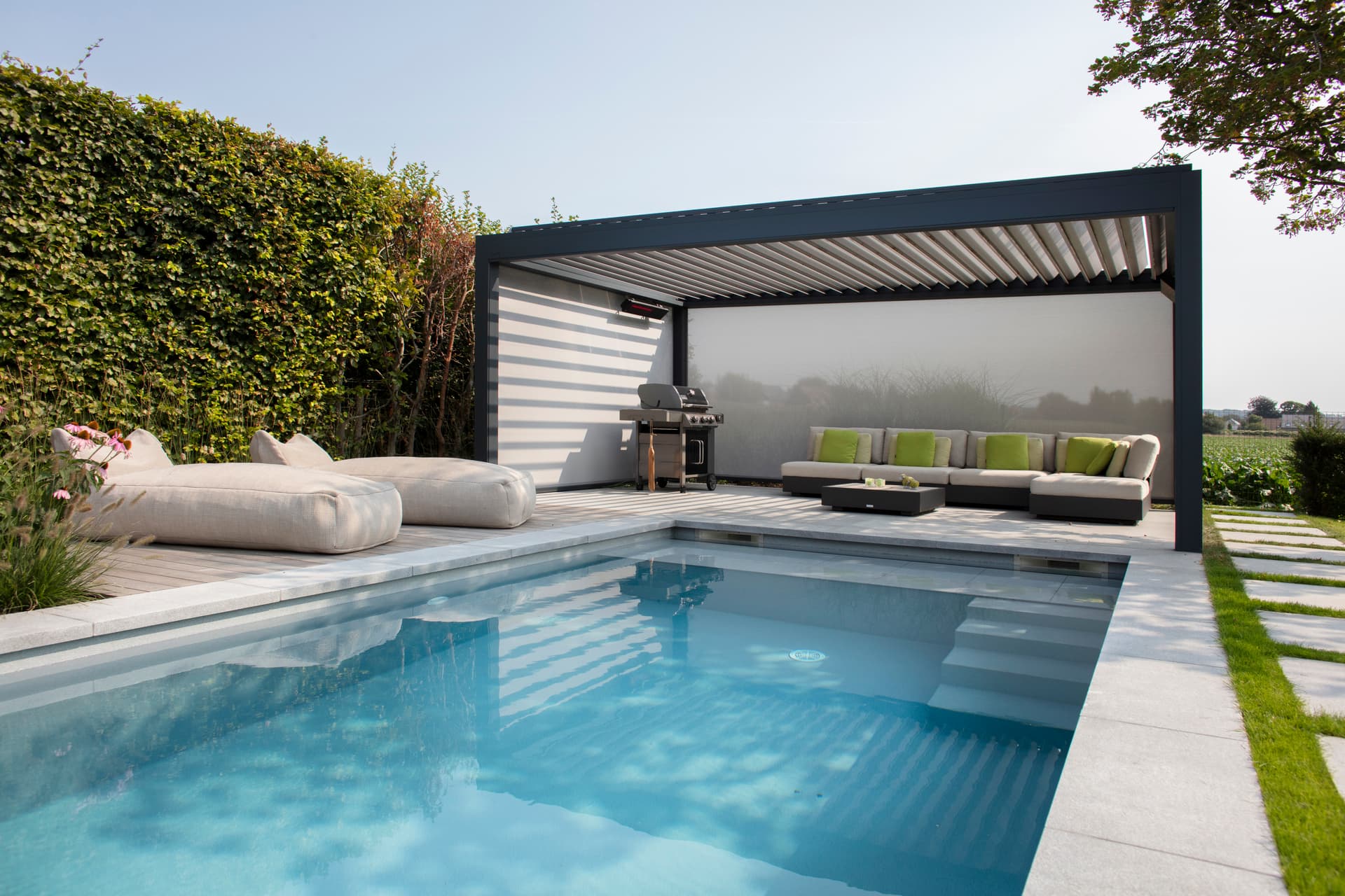 Aluminium louvred roof pergola in dark finish installed beside modern swimming pool and lounge area