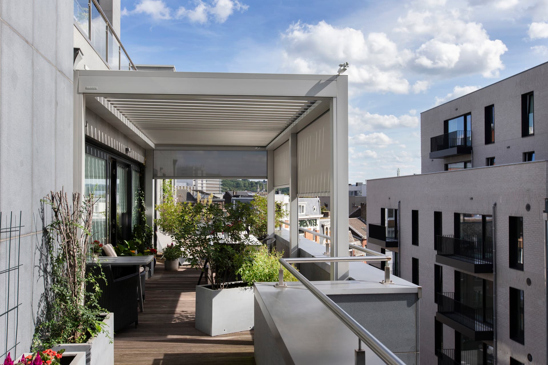 Aluminium pergola met lamellendak en ZIP‑screen op een balkonterras met uitzicht over de stad.