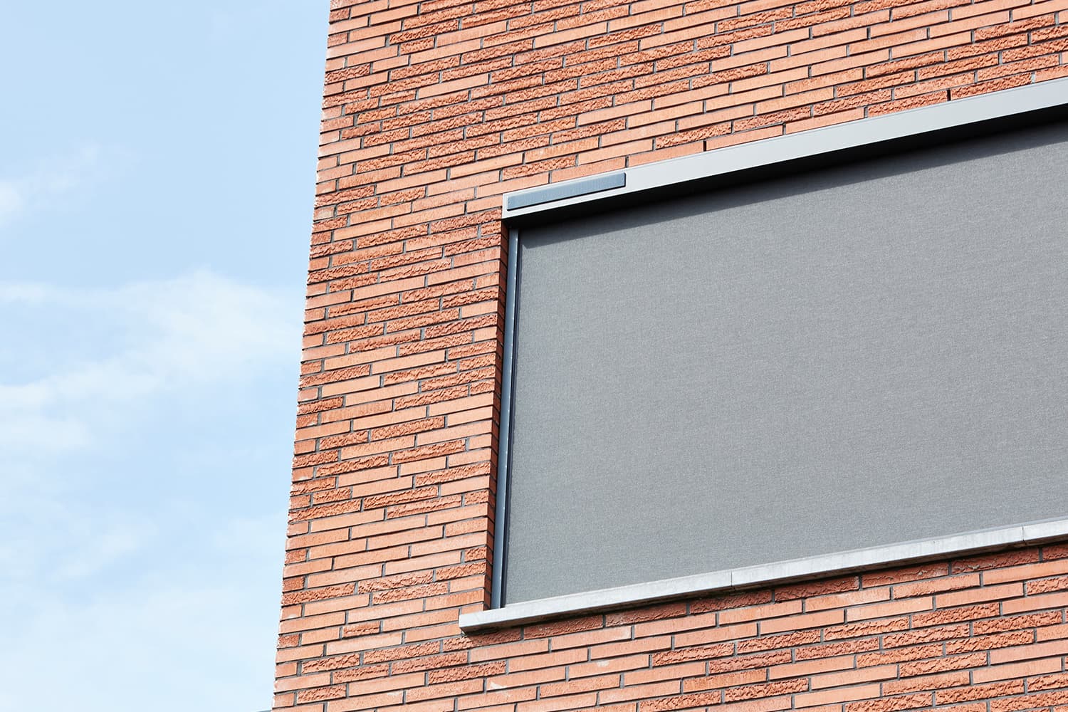 Aluminium zip screen in dark finish with integrated solar panel installed on modern brick façade window