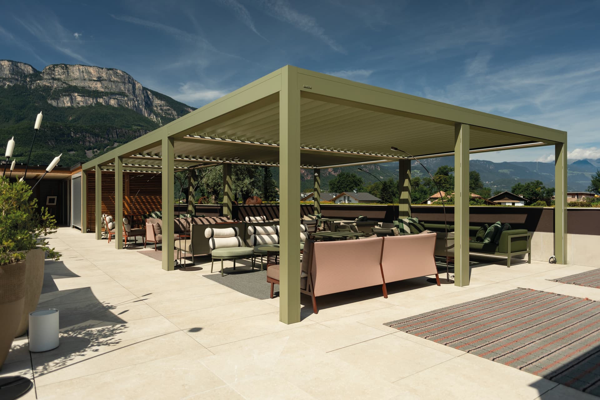 Aluminium pergola met lamellendak die een buitenlounge op een terras met uitzicht op de bergen overschaduwt.